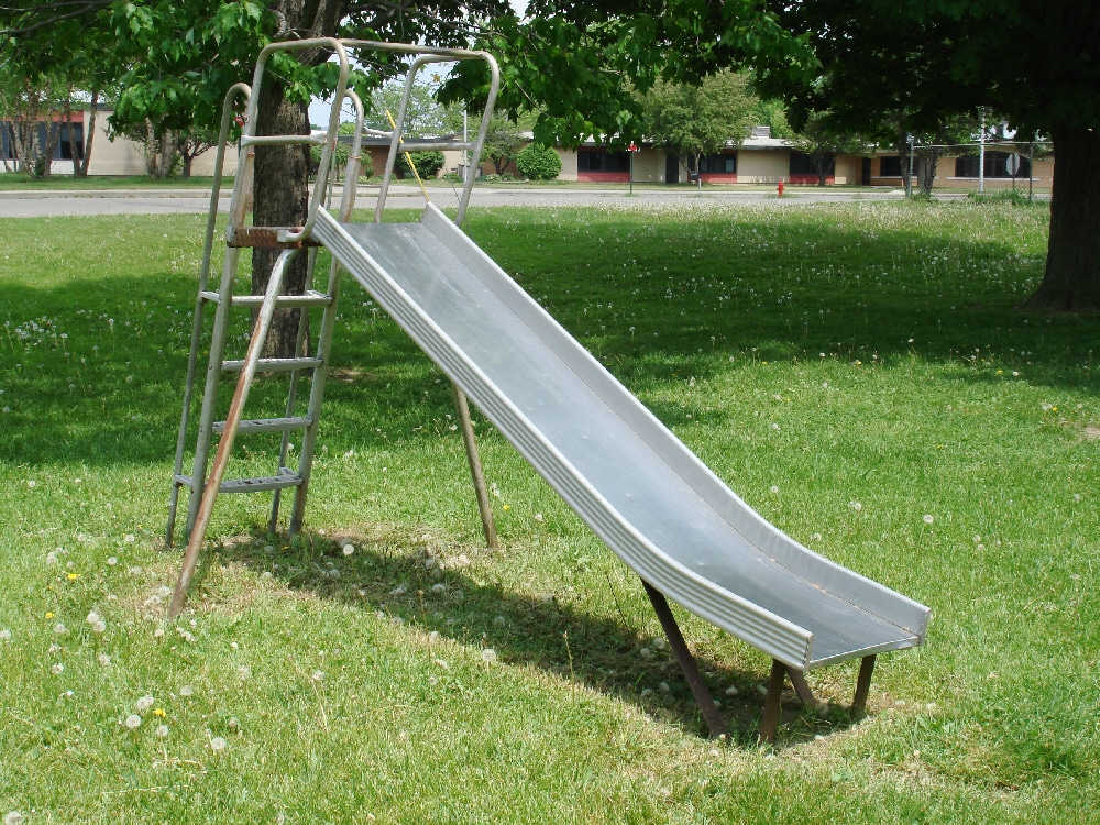 Metal playground slide above grass and worn ground