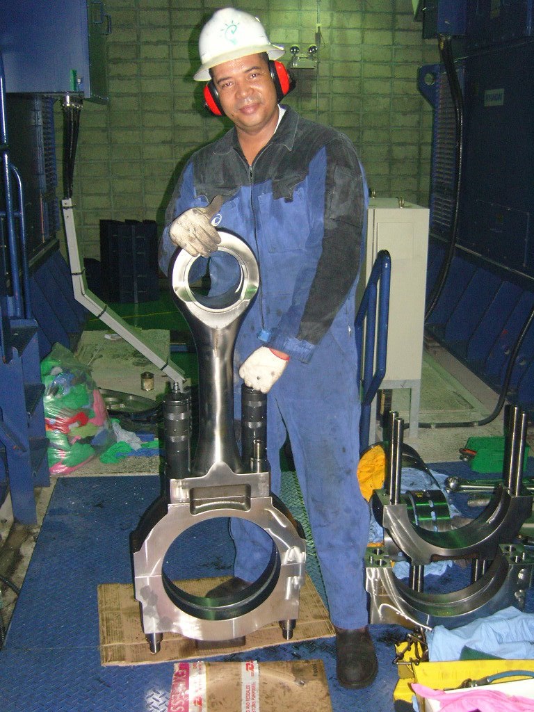 Power-plant mechanic holding a large connecting rod beside engine components