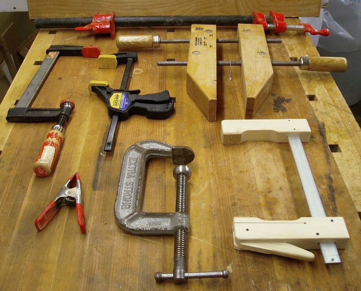 Several woodworking clamps, including a wooden handscrew, C-clamp, and bar clamps