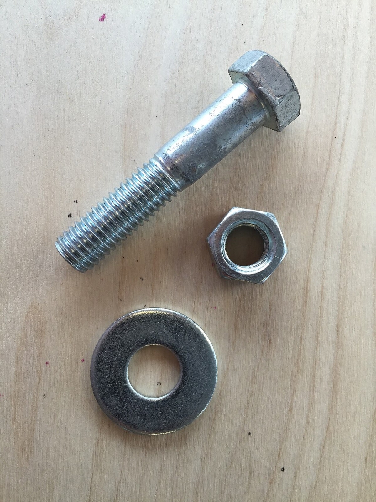 A steel bolt, nut, and flat washer on a wooden surface
