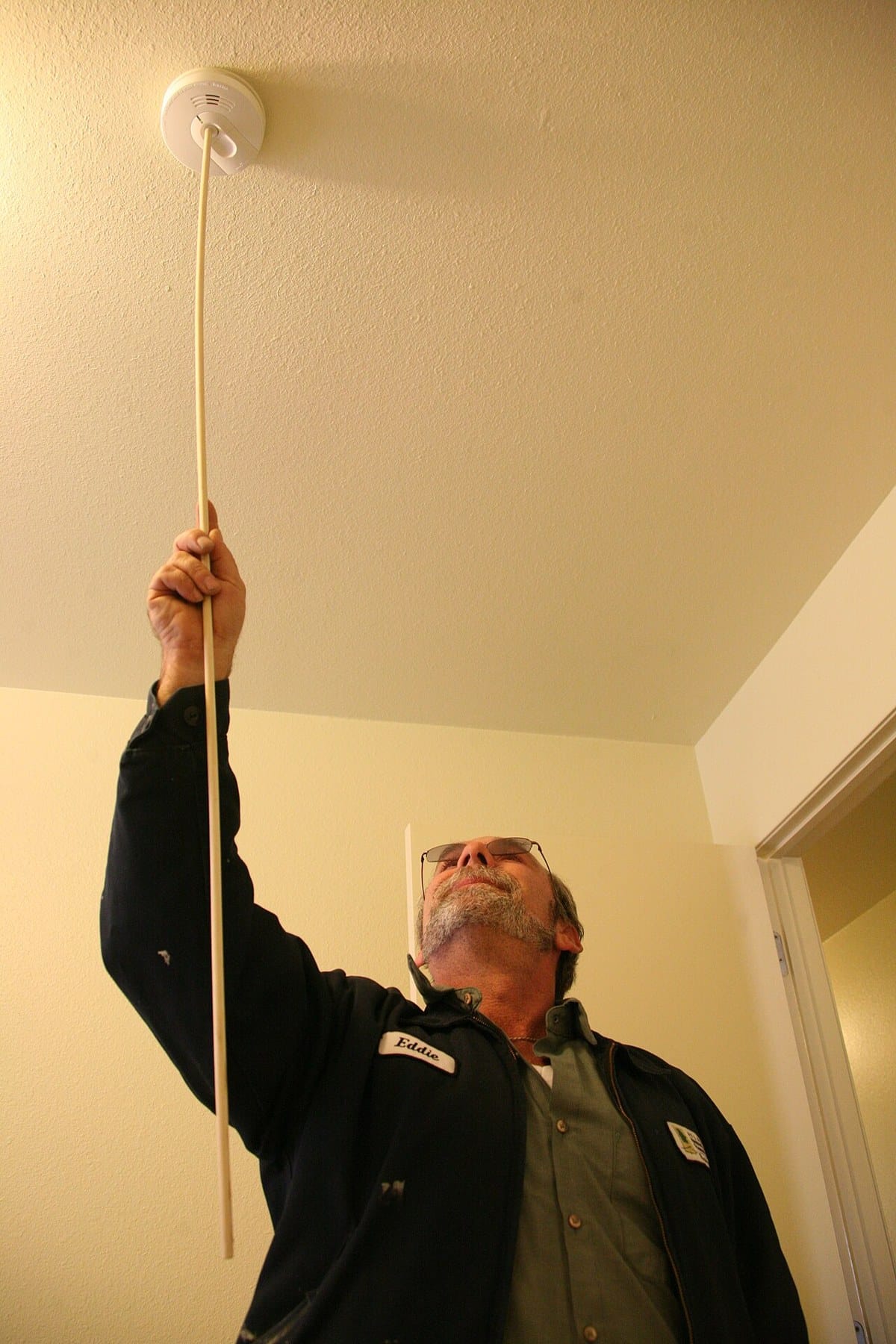 Maintenance technician checking a ceiling-mounted fire alarm