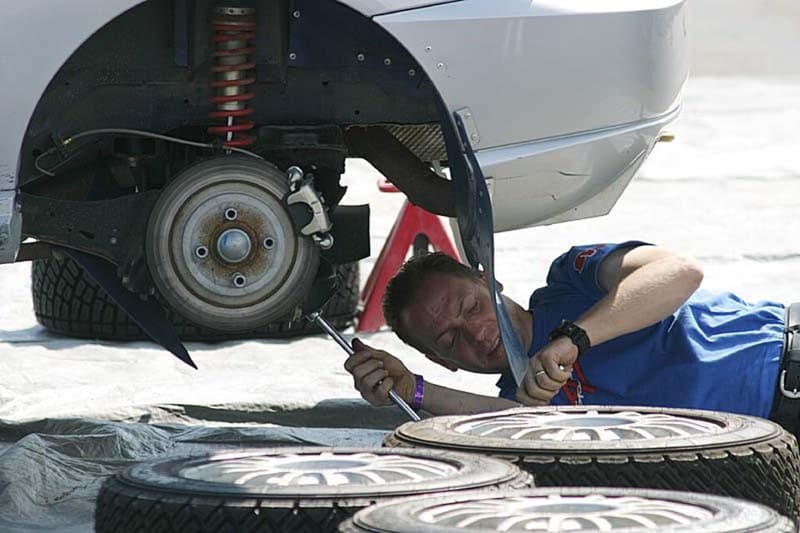 Mechanic working beneath a rally car with its wheel removed in Minnesota