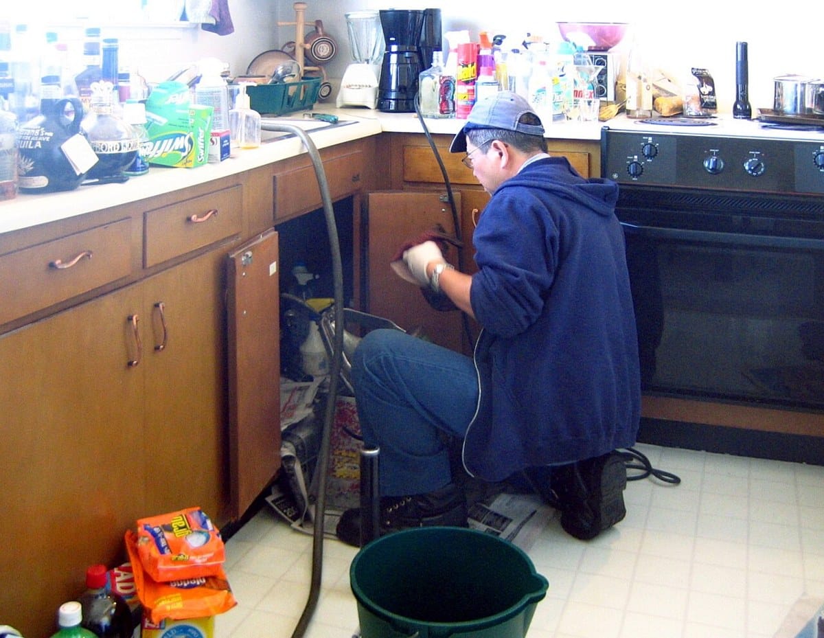 Plumber working on piping beneath a kitchen sink