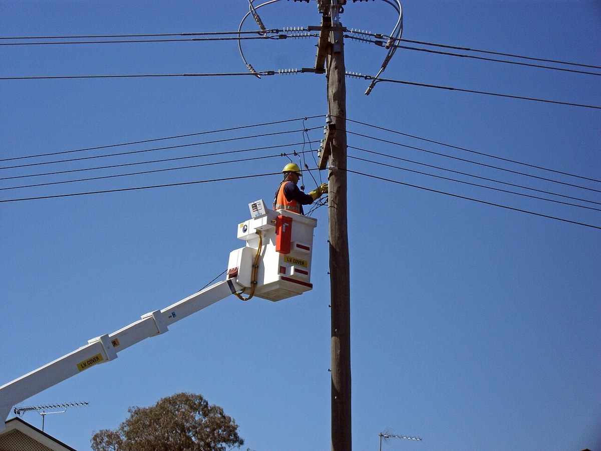 Electrical lineworker raised in a bucket beside power lines in Australia