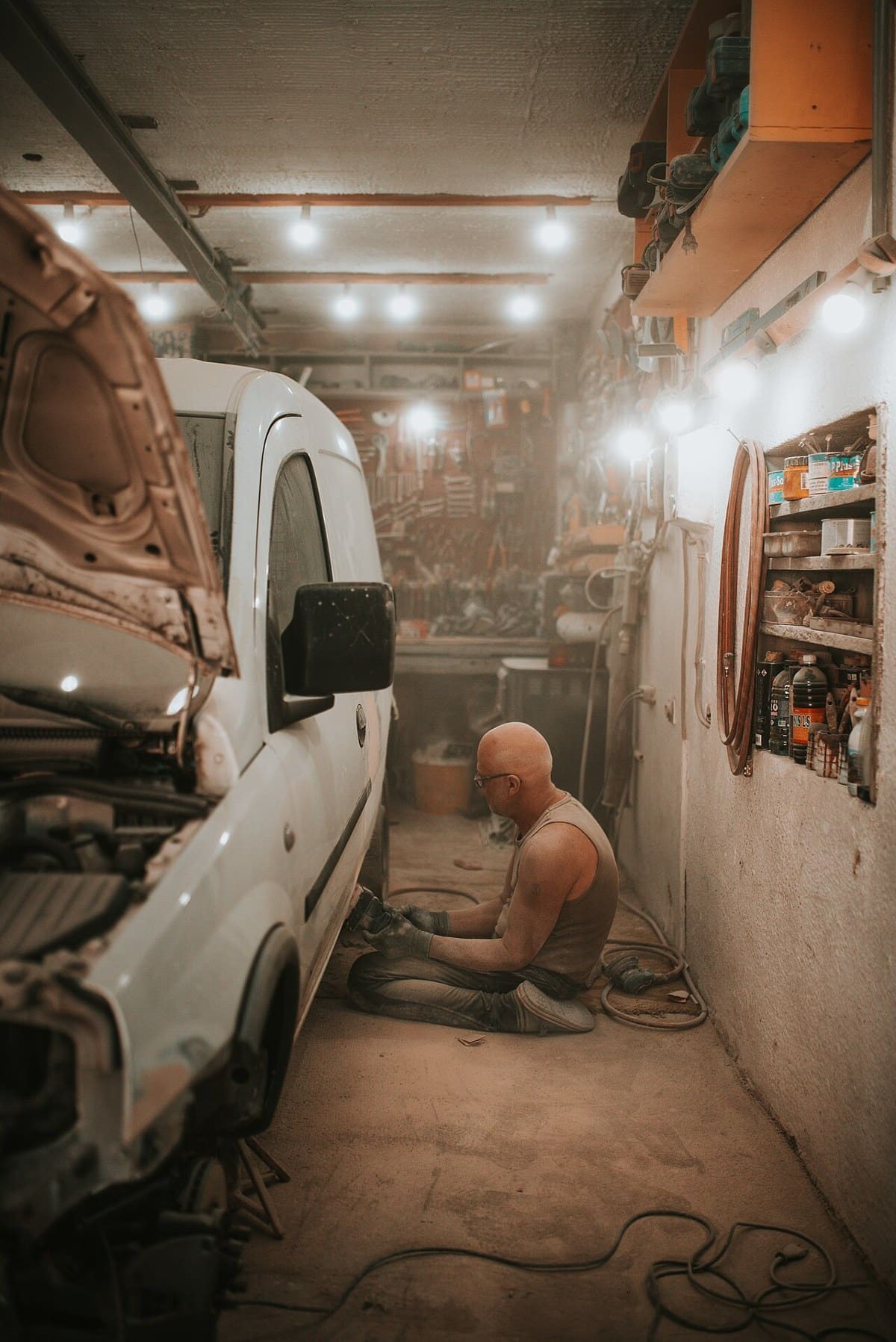 Worker sanding a vehicle body panel in a repair workshop