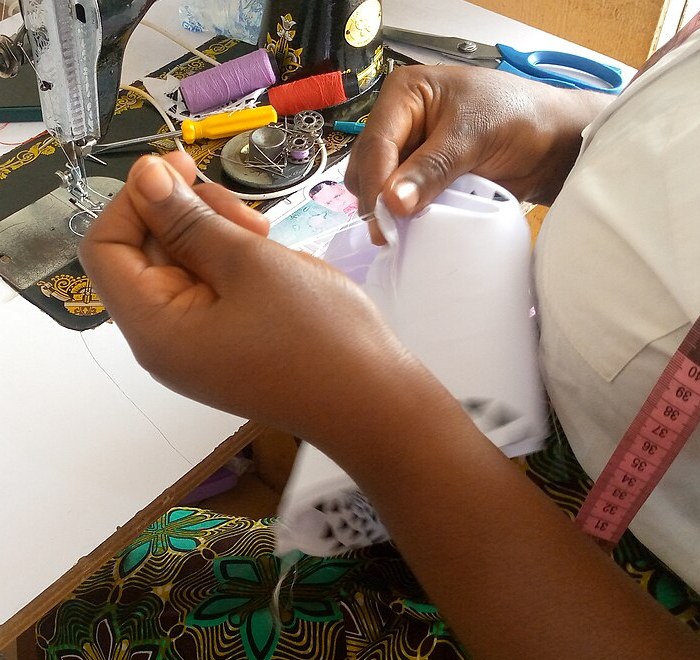 Hands using needle and thread to sew a button onto a garment