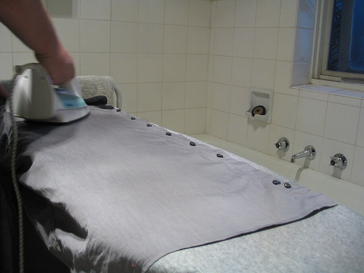 A hand guiding an iron over a shirt on an ironing board