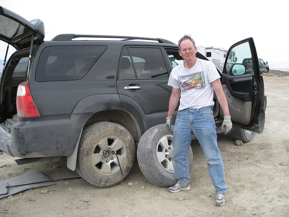 Man beside a Toyota SUV during a tire change, with a spare wheel and lug wrench