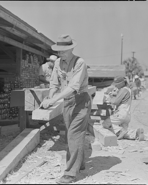 A carpenter uses a hand plane on a timber at a shipyard in 1942