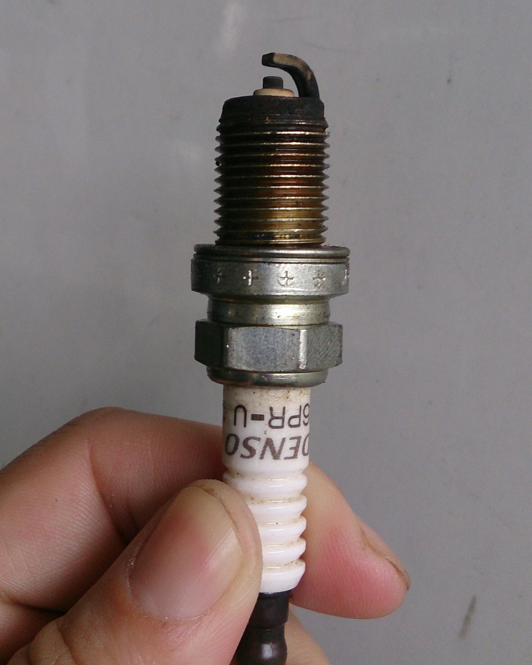 A hand holds a used spark plug with its electrode visible
