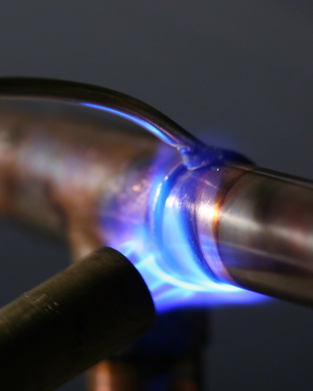 A torch heats a copper pipe fitting while solder touches the joint